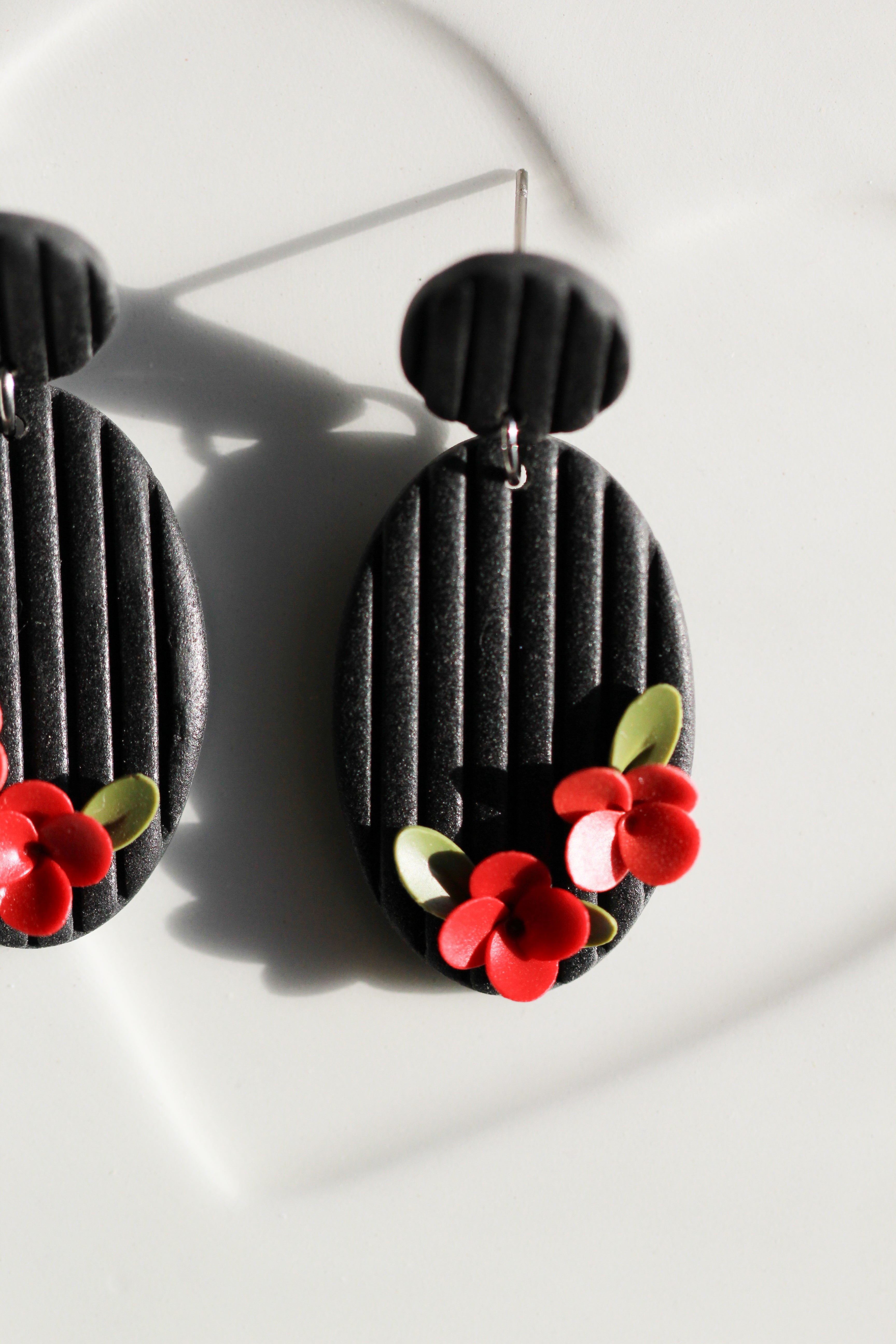 Black earrings with red floral designs on a white background