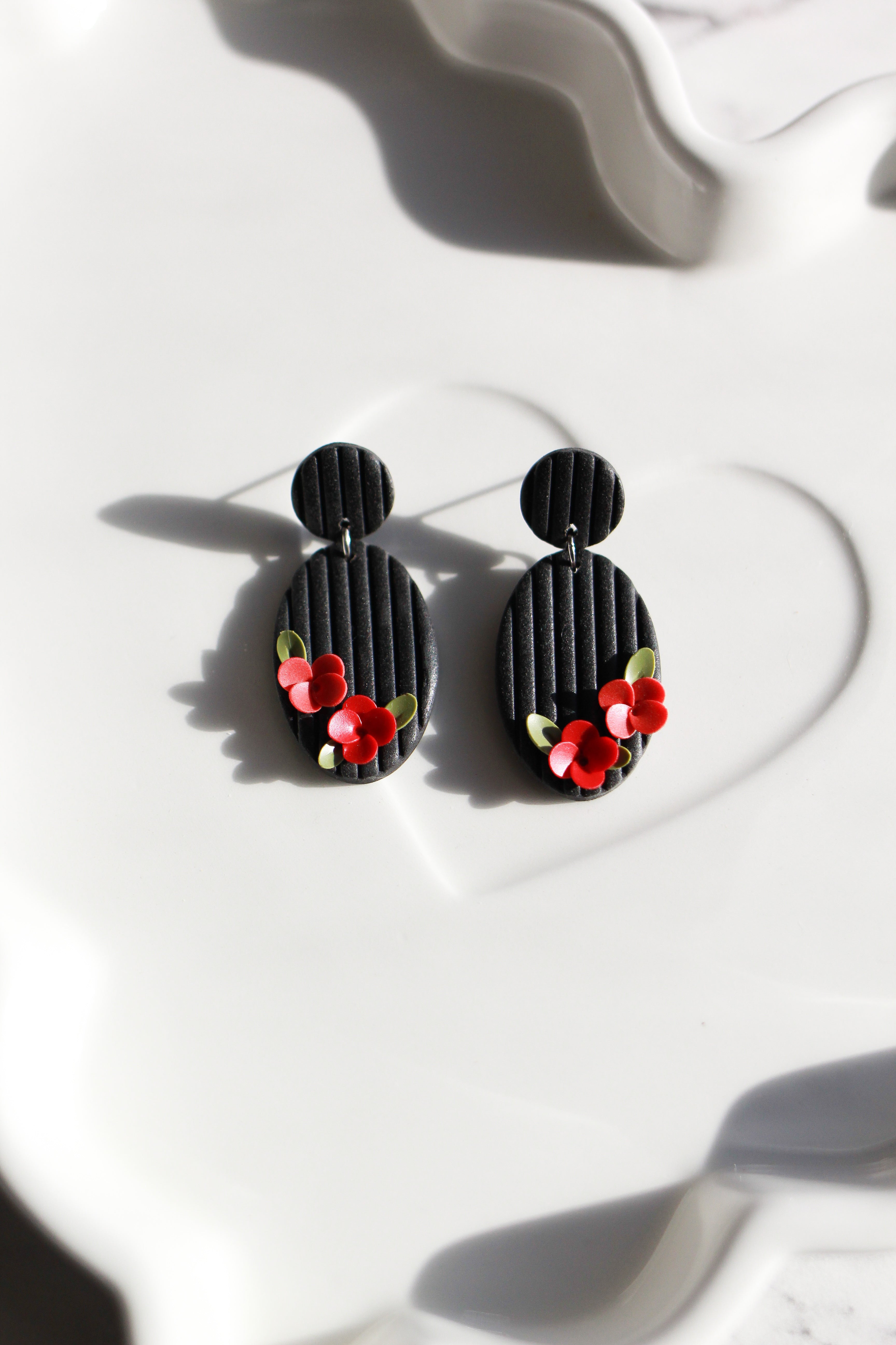 Black earrings with red floral details on a white surface
