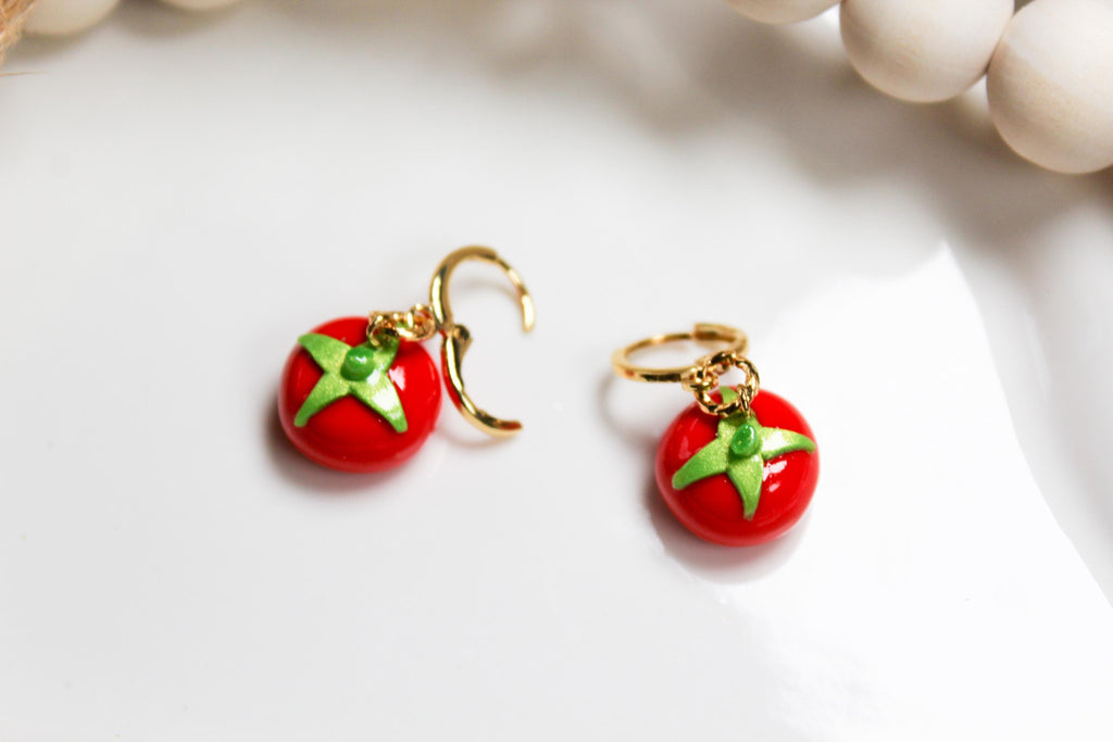 Red tomato-shaped earrings with green leaves on a white surface