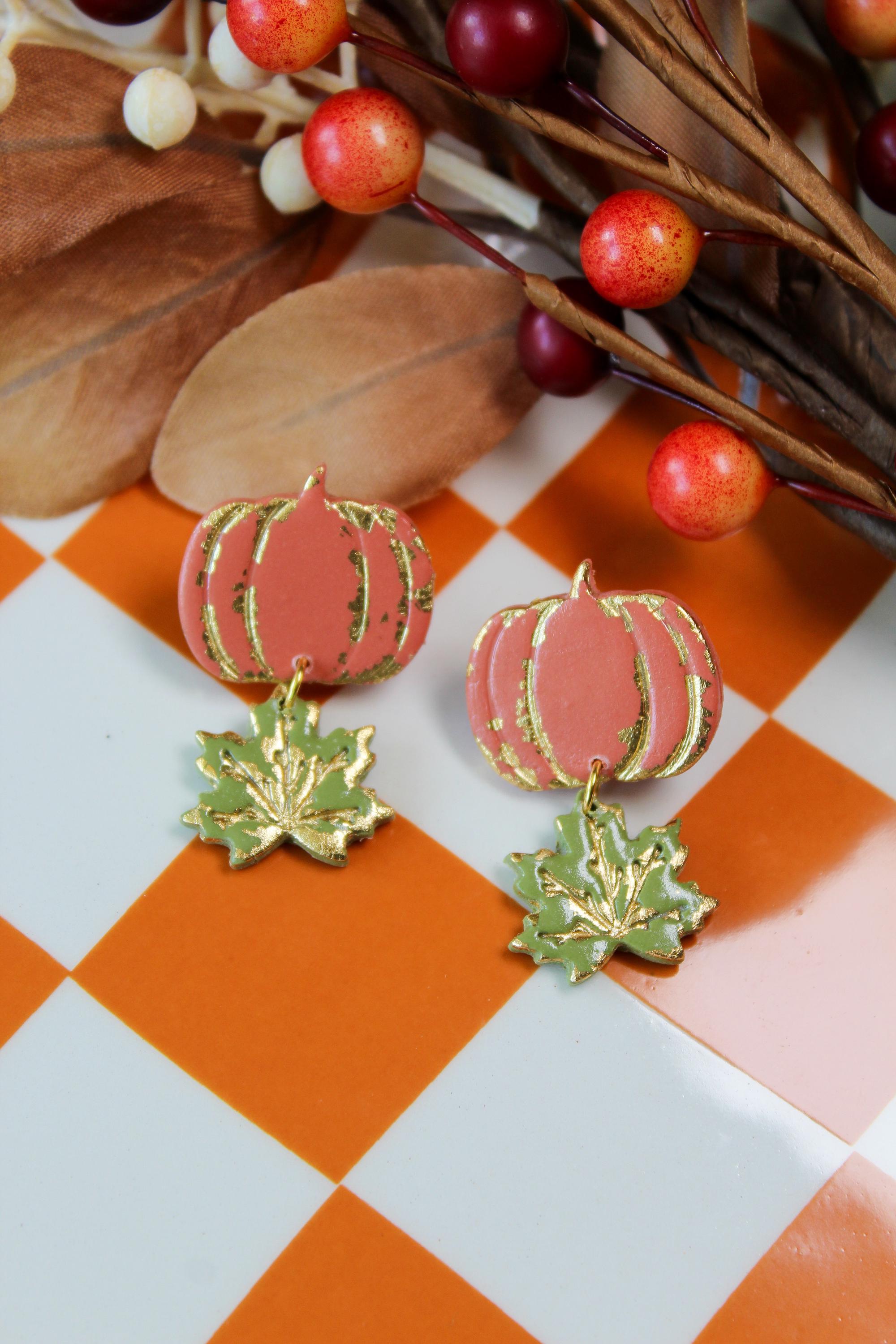 Pumpkin-shaped and leaf earrings with gold accents on a checkered background