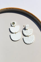 White ceramic earrings with gold accents on a light gray surface.