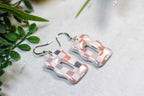Pair of earrings with a geometric pattern on a light surface with green leaves.