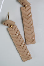 Pair of beige zigzag patterned earrings on a white background