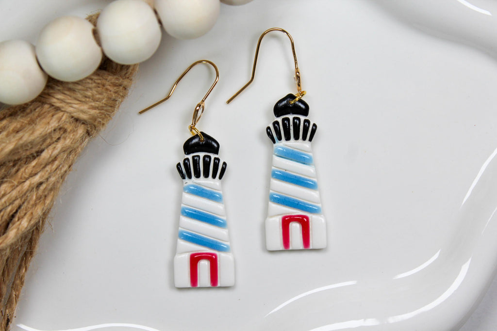 Lighthouse-shaped earrings on a white plate with beads and twine.