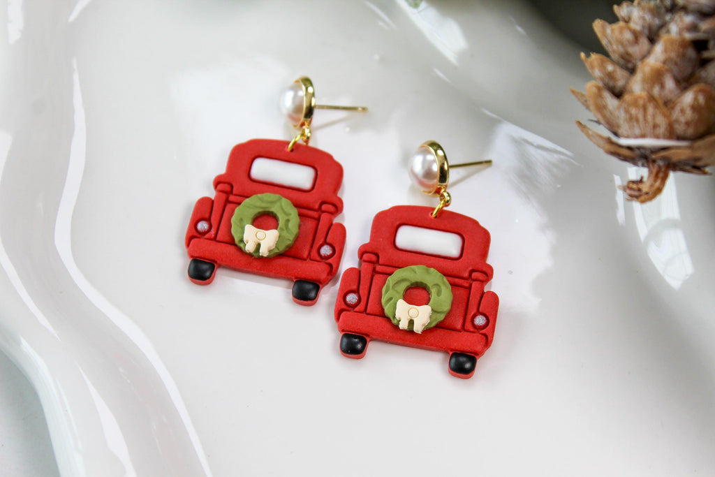 Red truck-shaped earrings with green wreaths on a white dish.