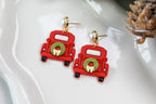 Red truck-shaped earrings with green wreaths on a white dish.