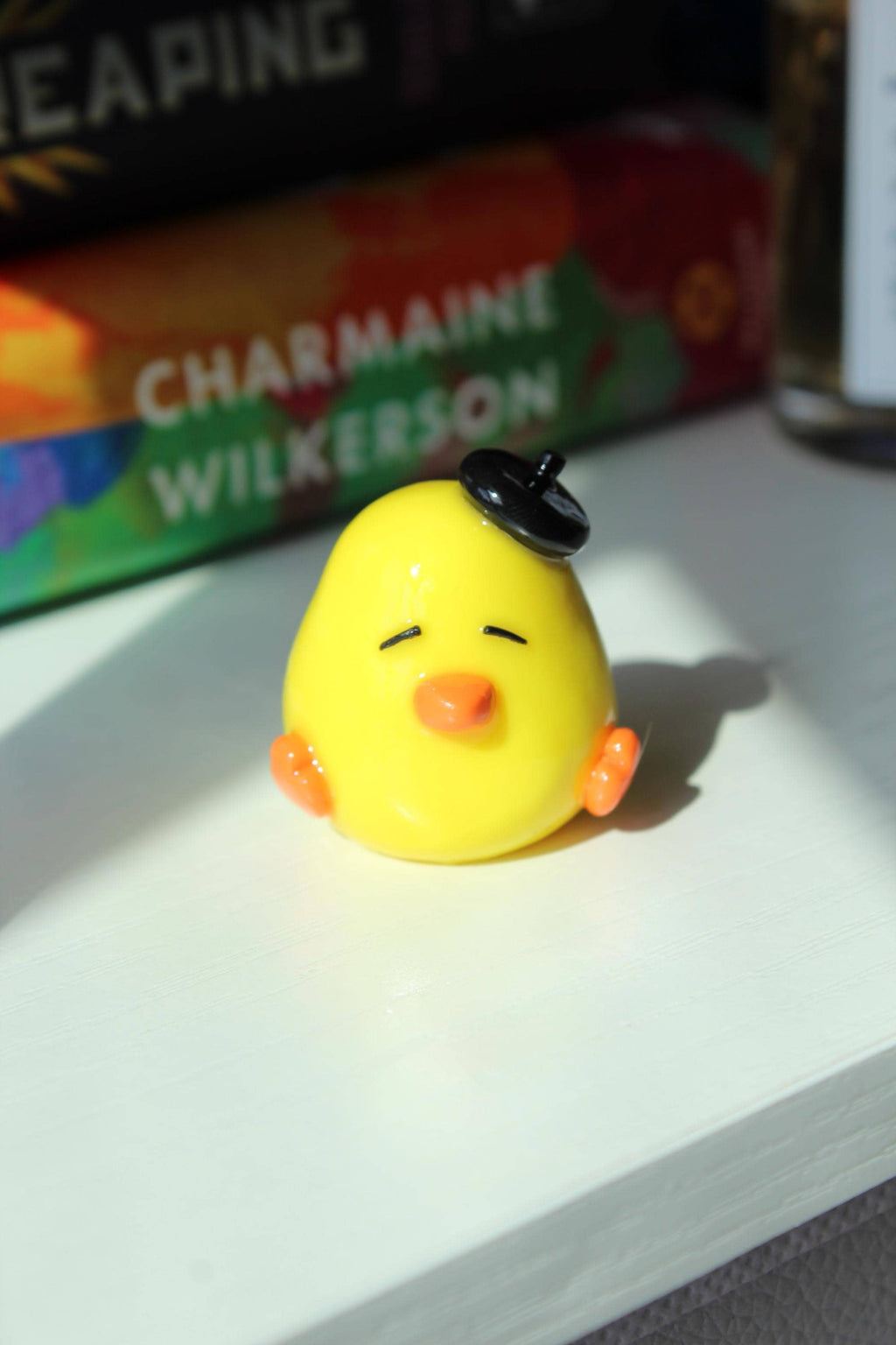 Yellow duck with a black hat on a white surface, with books in the background.