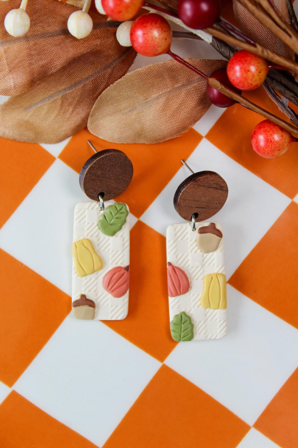 Wooden earrings with colorful autumn designs on a checkered orange and white background.