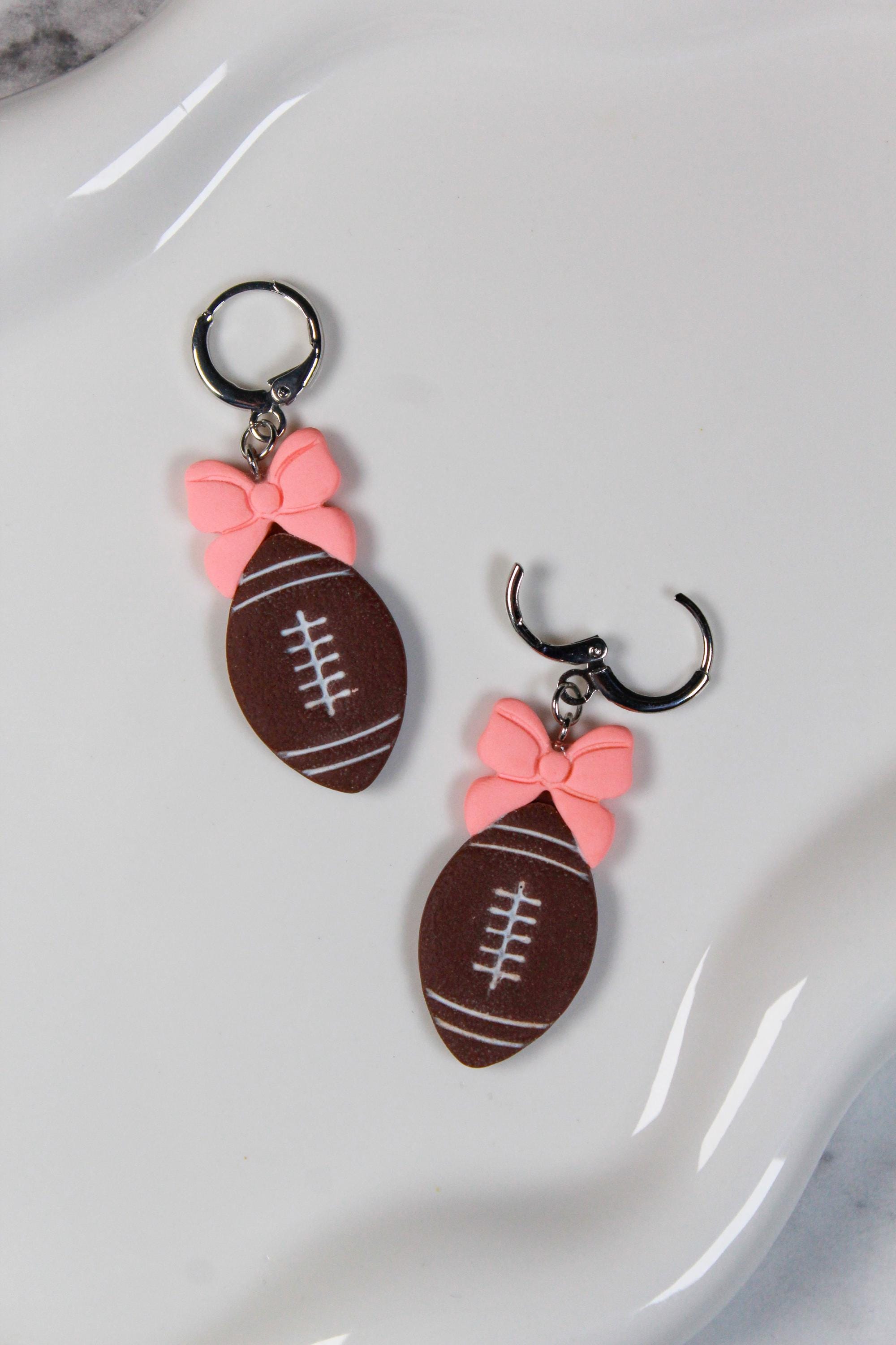 Football-shaped earrings with pink bows on a white surface