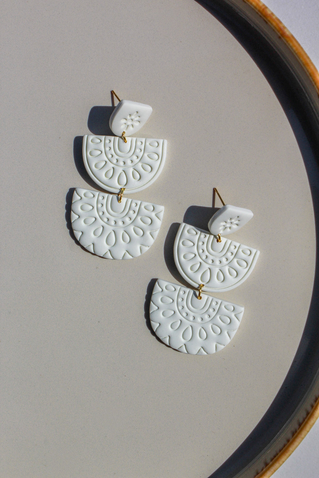 White ceramic earrings with gold accents on a beige surface