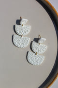 White ceramic earrings with gold accents on a beige surface