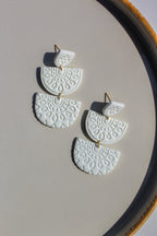 White ceramic earrings with gold accents on a beige surface