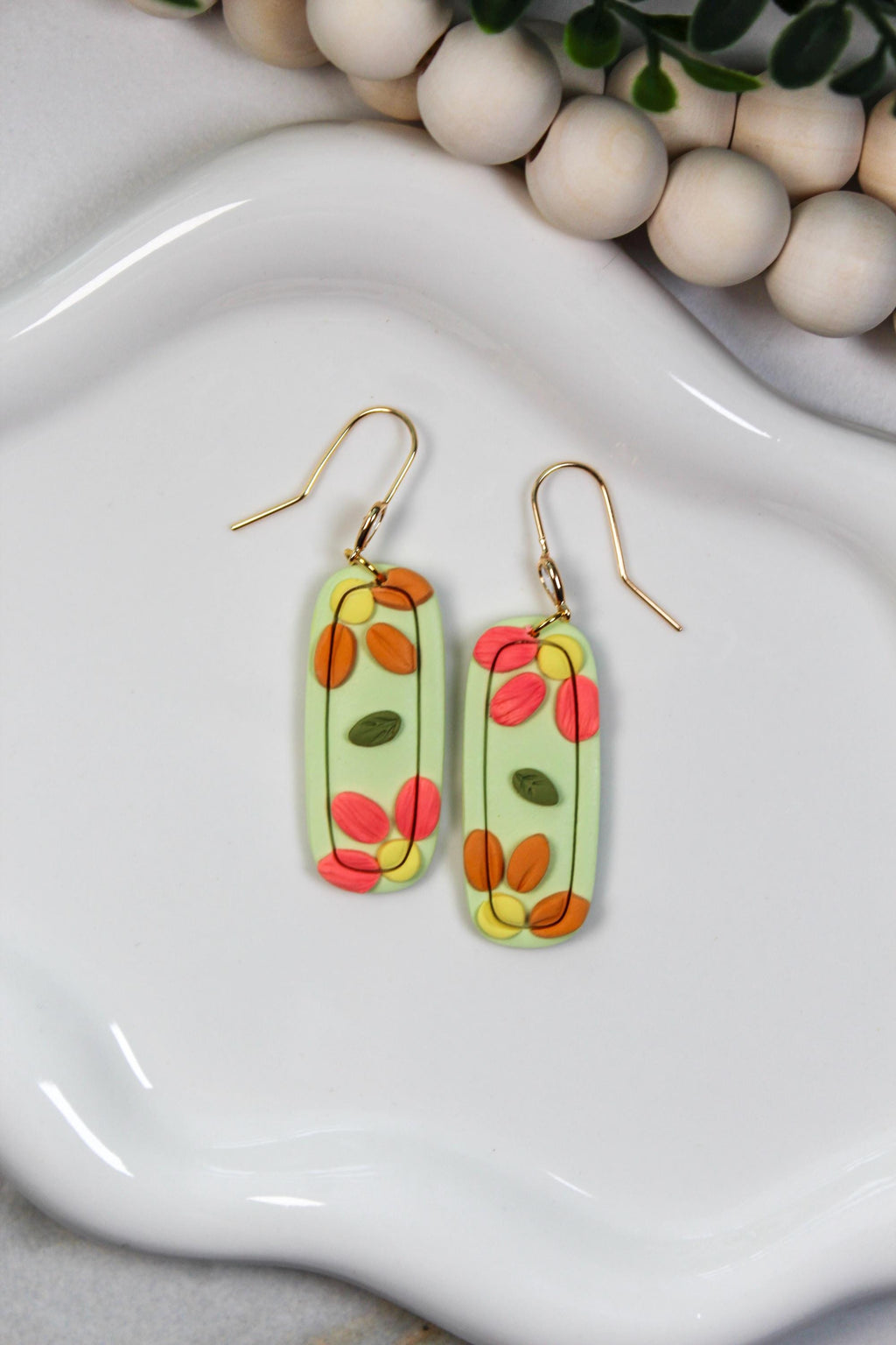 Colorful oval-shaped earrings on a white dish with wooden beads in the background