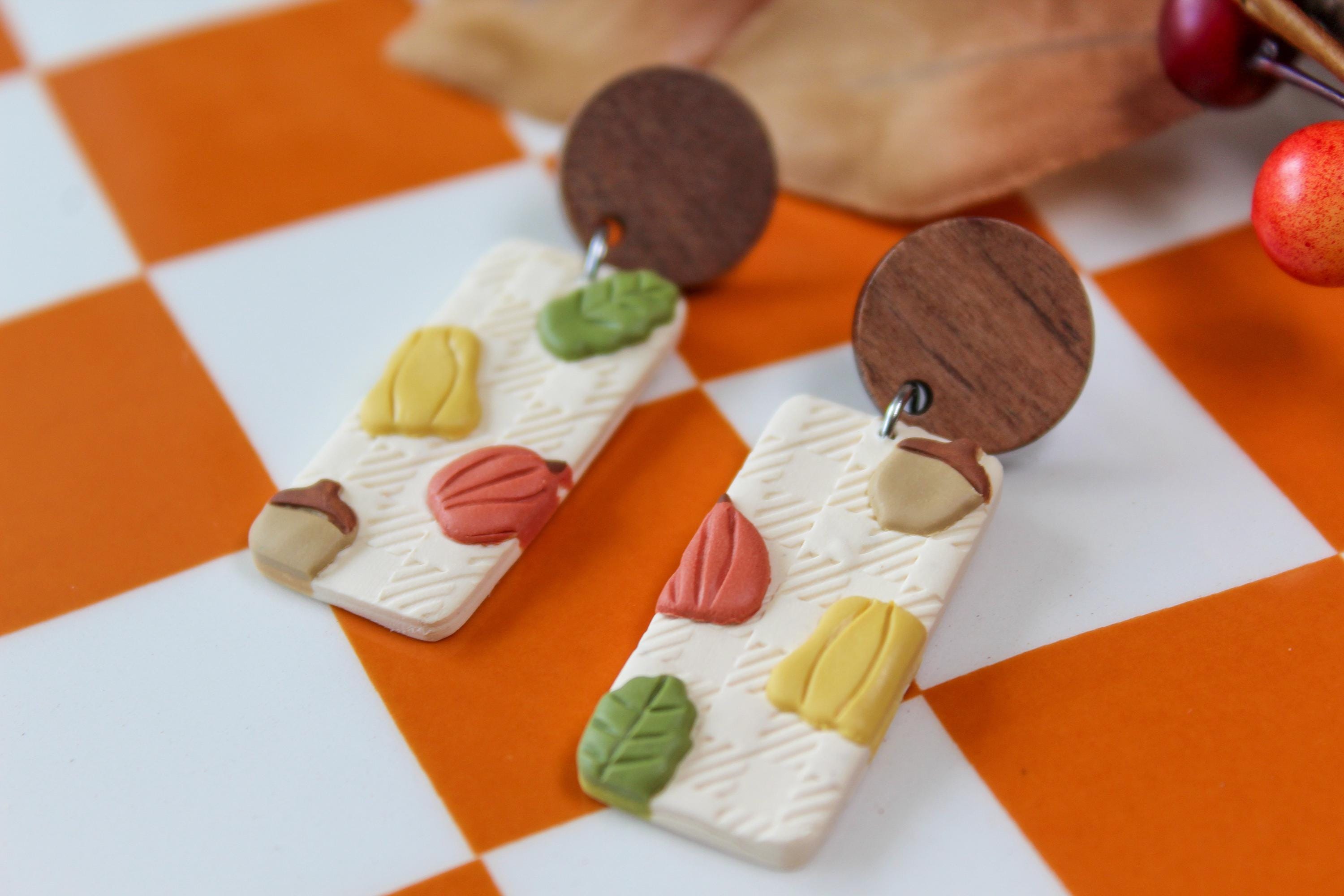 Wooden earrings with colorful autumn designs on a checkered orange and white background.