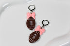 Football-shaped earrings with pink bows on a white surface
