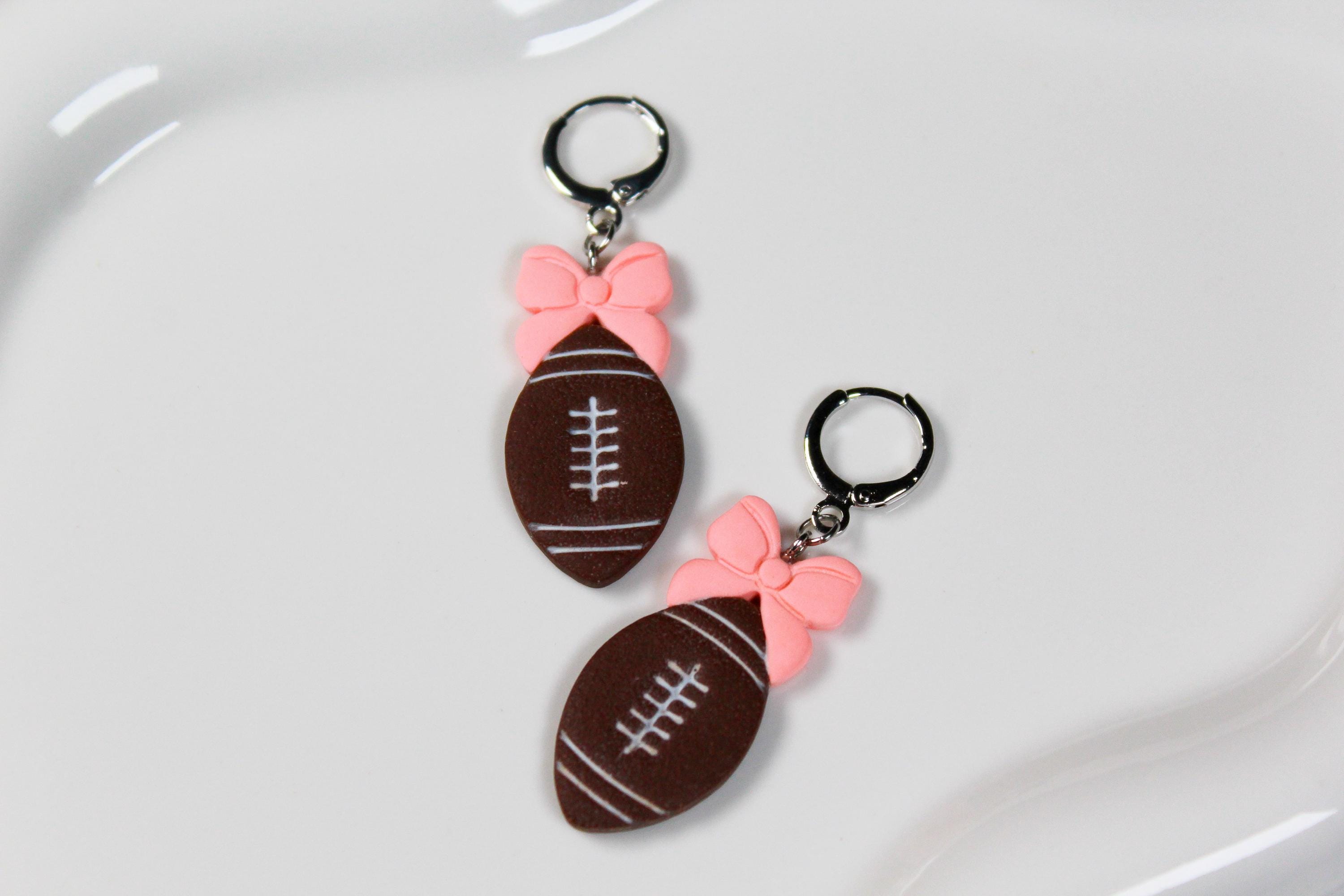 Football-shaped earrings with pink bows on a white surface