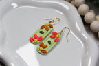 Colorful floral earrings on a white dish with beads in the background