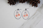 Pair of earrings with floral design on a white surface with pine cones.