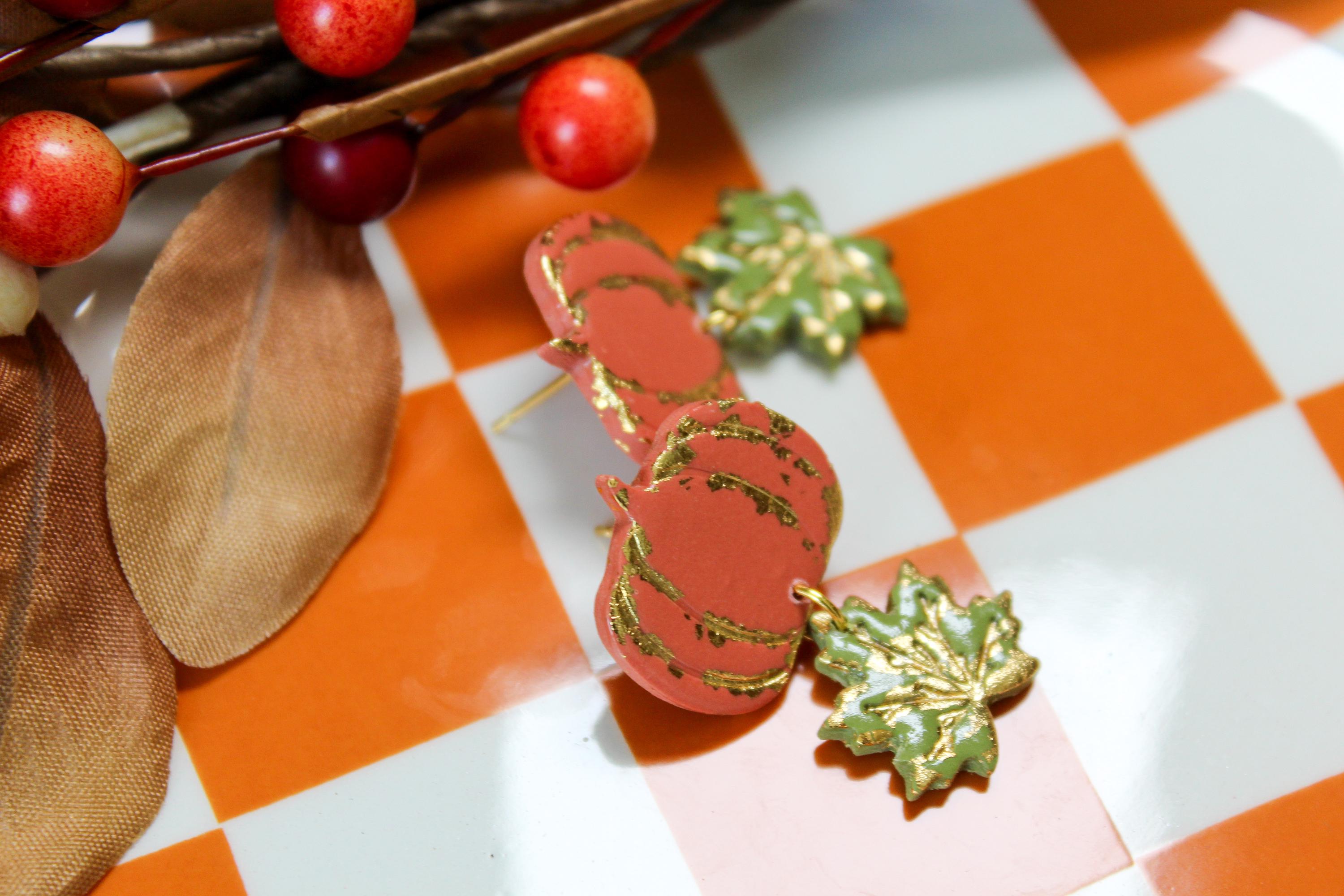 Pumpkin-shaped and leaf earrings with gold accents on a checkered background