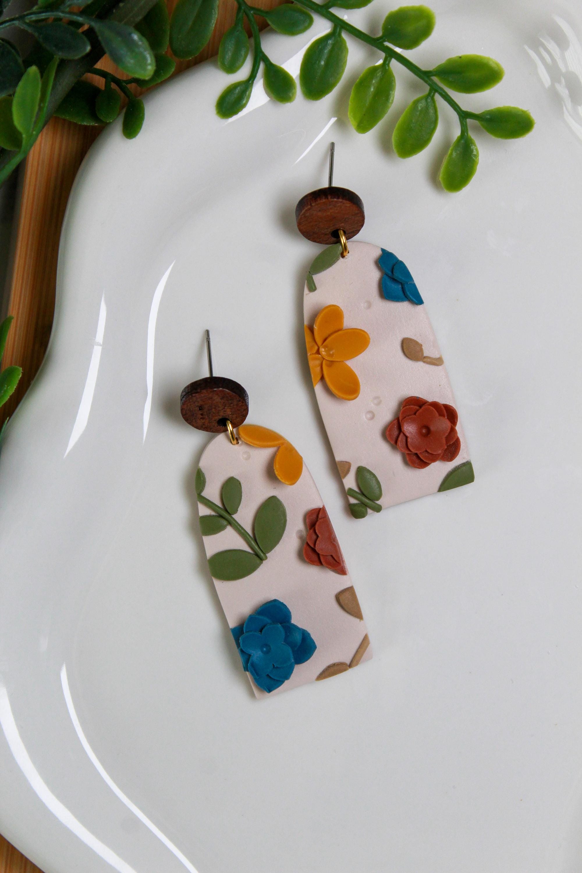 Floral patterned earrings on a white plate with green leaves in the background