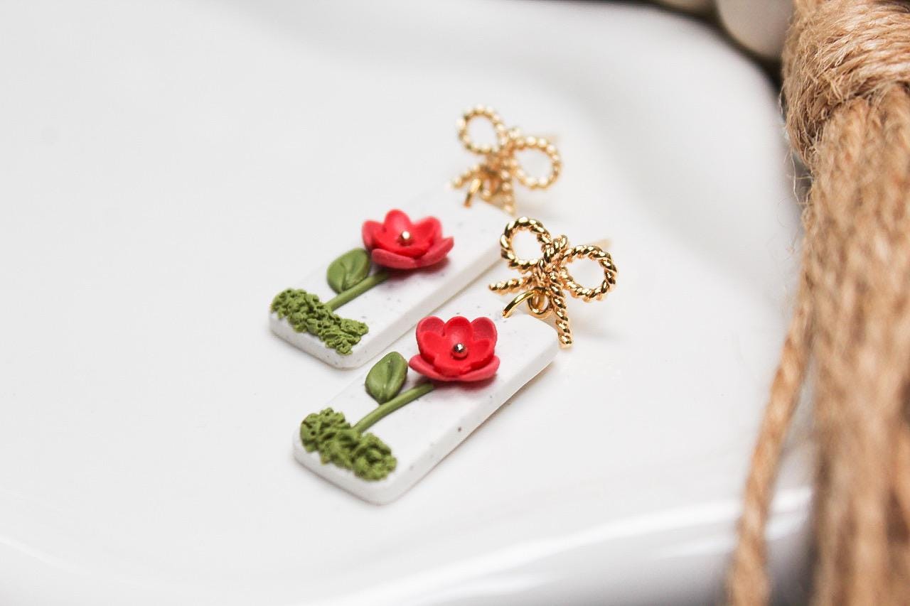 Floral-themed earrings on a white surface with a blurred background