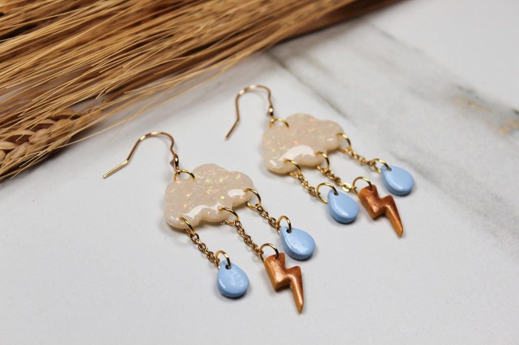 Pair of earrings with cloud and lightning bolt designs on a light surface.