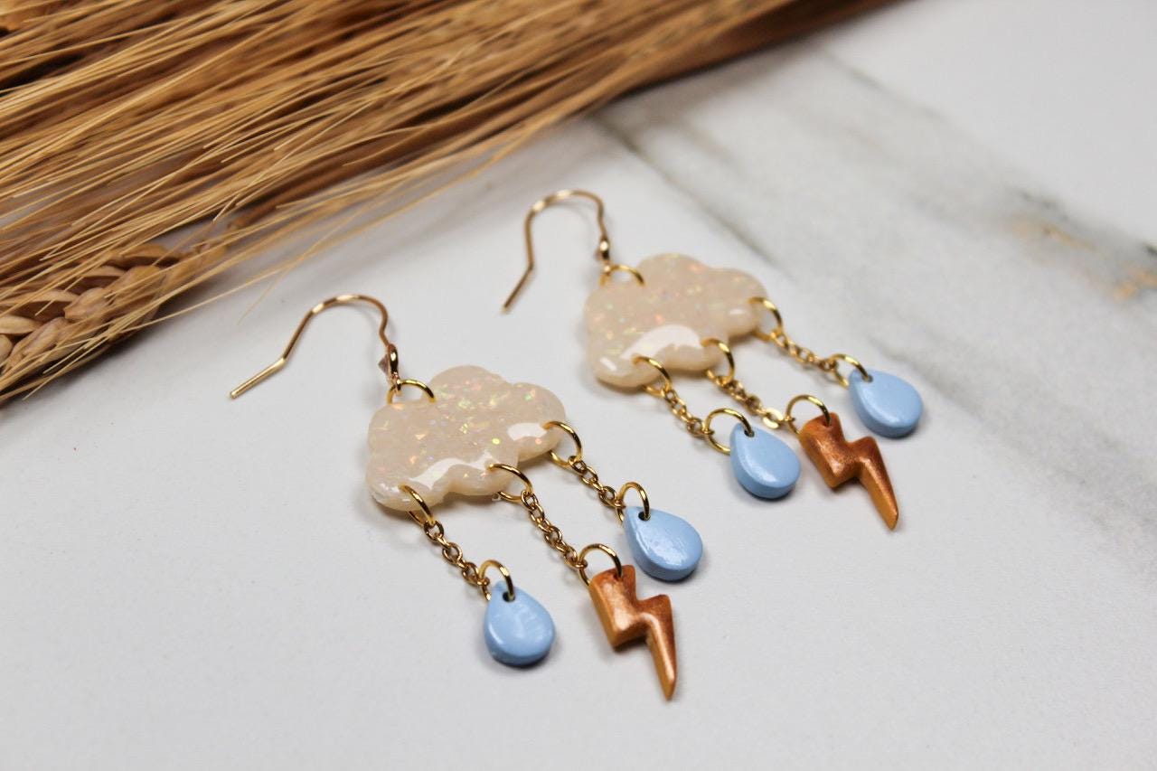 Pair of earrings with cloud and lightning bolt designs on a light surface.