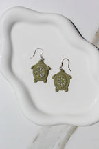 Green turtle-shaped earrings on a white ceramic dish.