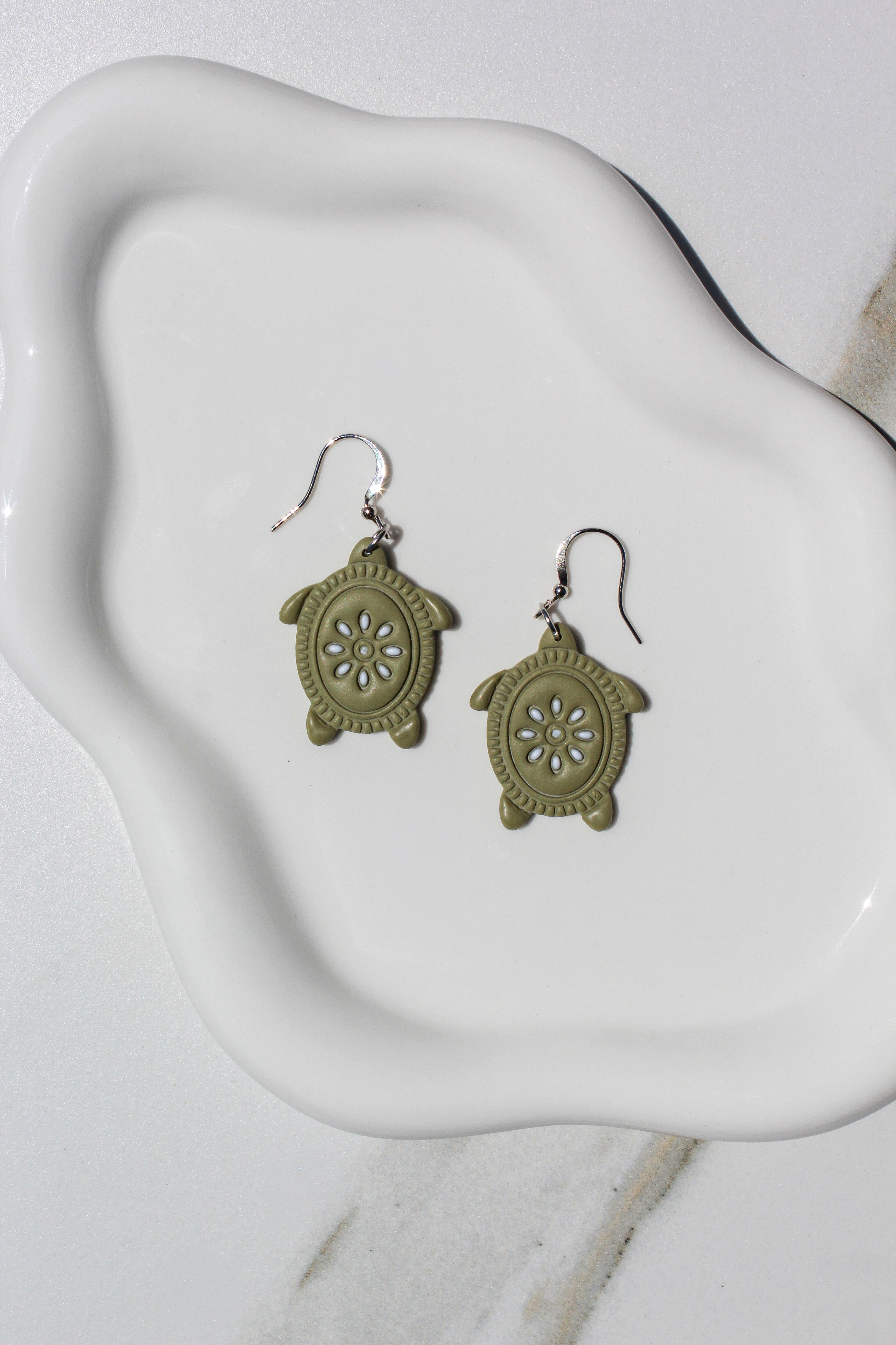 Green turtle-shaped earrings on a white ceramic dish.