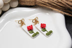 Floral earrings with red flowers and green leaves on a white dish.