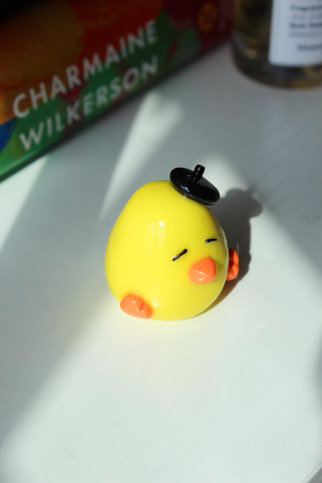 Yellow duck with a black hat on a white surface, with books in the background.