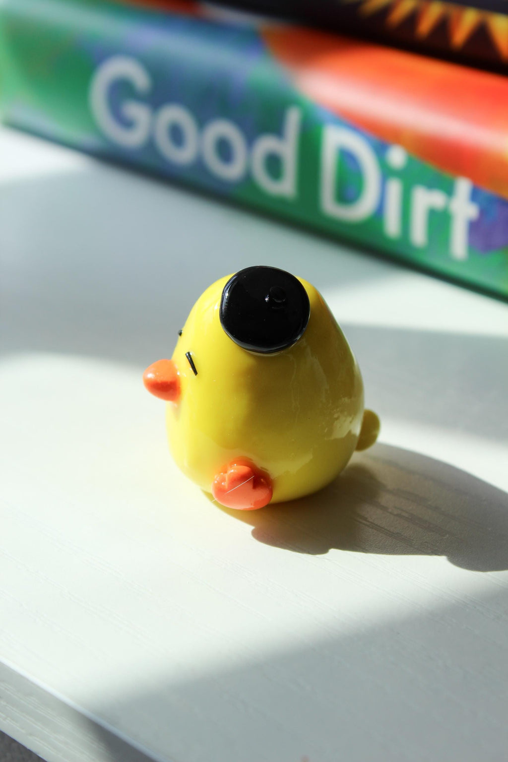 Yellow duck with a black hat on a white surface, with books in the background.
