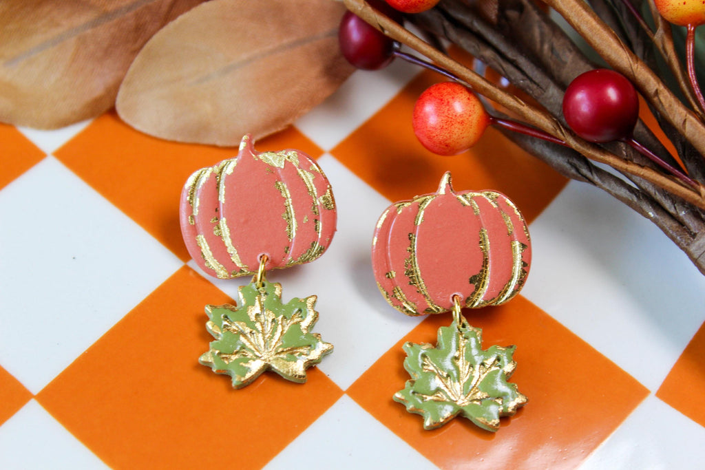 Pumpkin-shaped and leaf earrings with gold accents on a checkered background