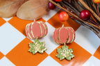 Pumpkin-shaped and leaf earrings with gold accents on a checkered background