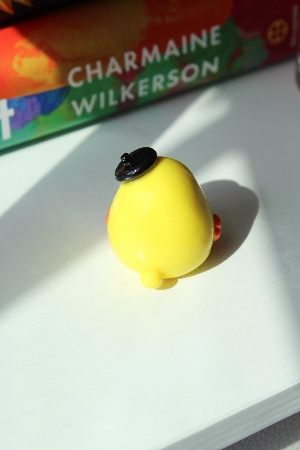 Yellow duck with a black hat on a white surface, with books in the background.