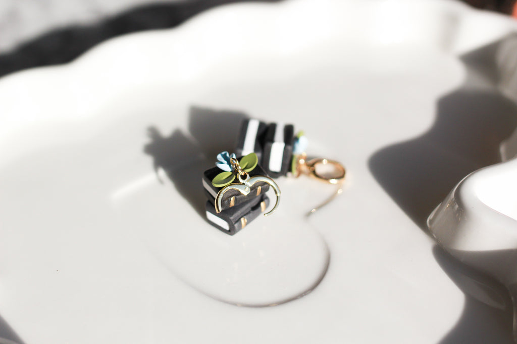 Close-up of black and white book earrings with huggie accessory on a white surface