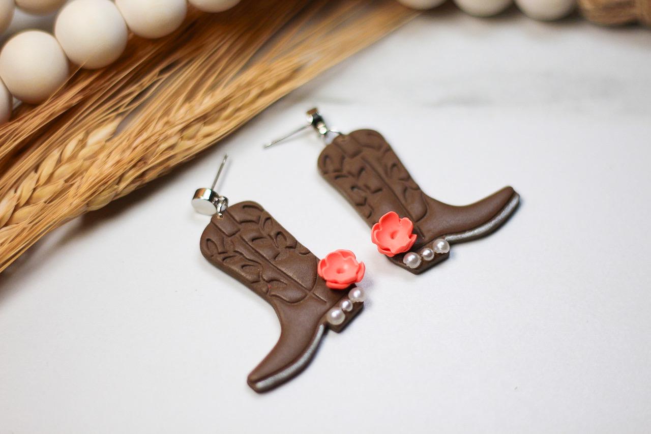 Brown cowboy boot earrings with pink flowers on a light background