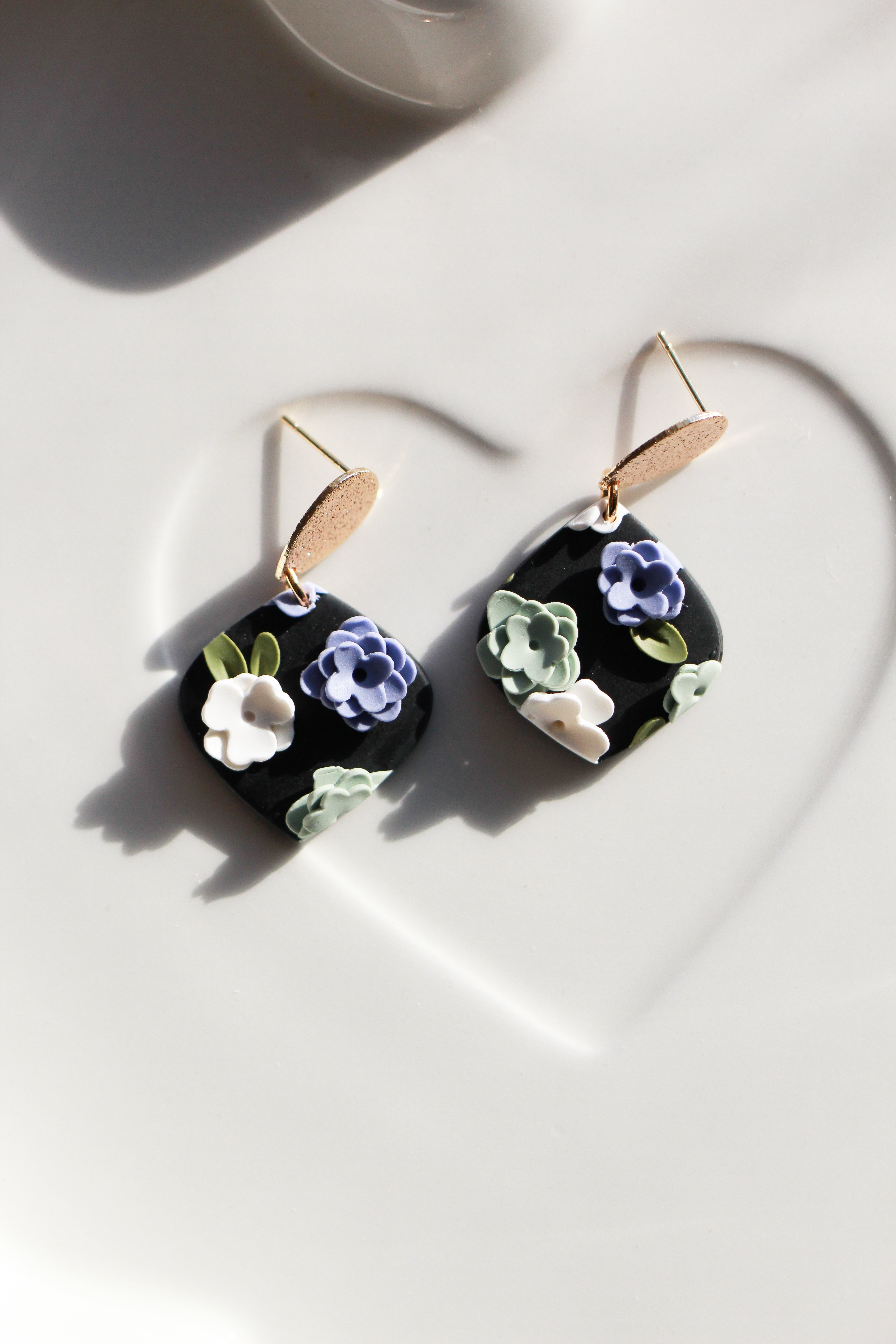 Floral earrings on a white surface with a heart-shaped shadow