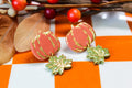 Pumpkin-shaped and leaf earrings with gold accents on a checkered background