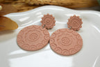 Pair of pink earrings with floral patterns on a white dish.