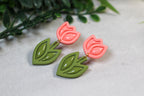 Pair of pink tulip-shaped earrings with green leaf details on a light gray surface.