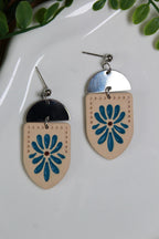 Pair of earrings with floral design on a white plate with green leaves.