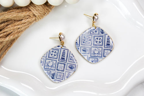Pair of blue and white patterned earrings on a white surface with a beige woven mat.