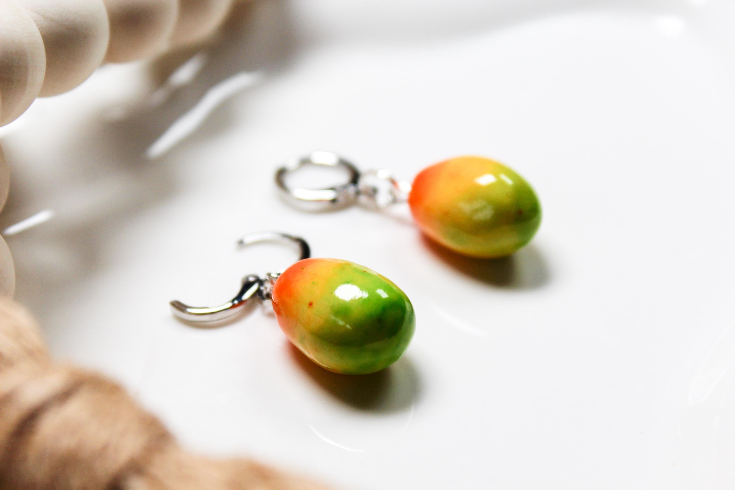 Pair of colorful mango-shaped earrings on a white surface with a blurred background.