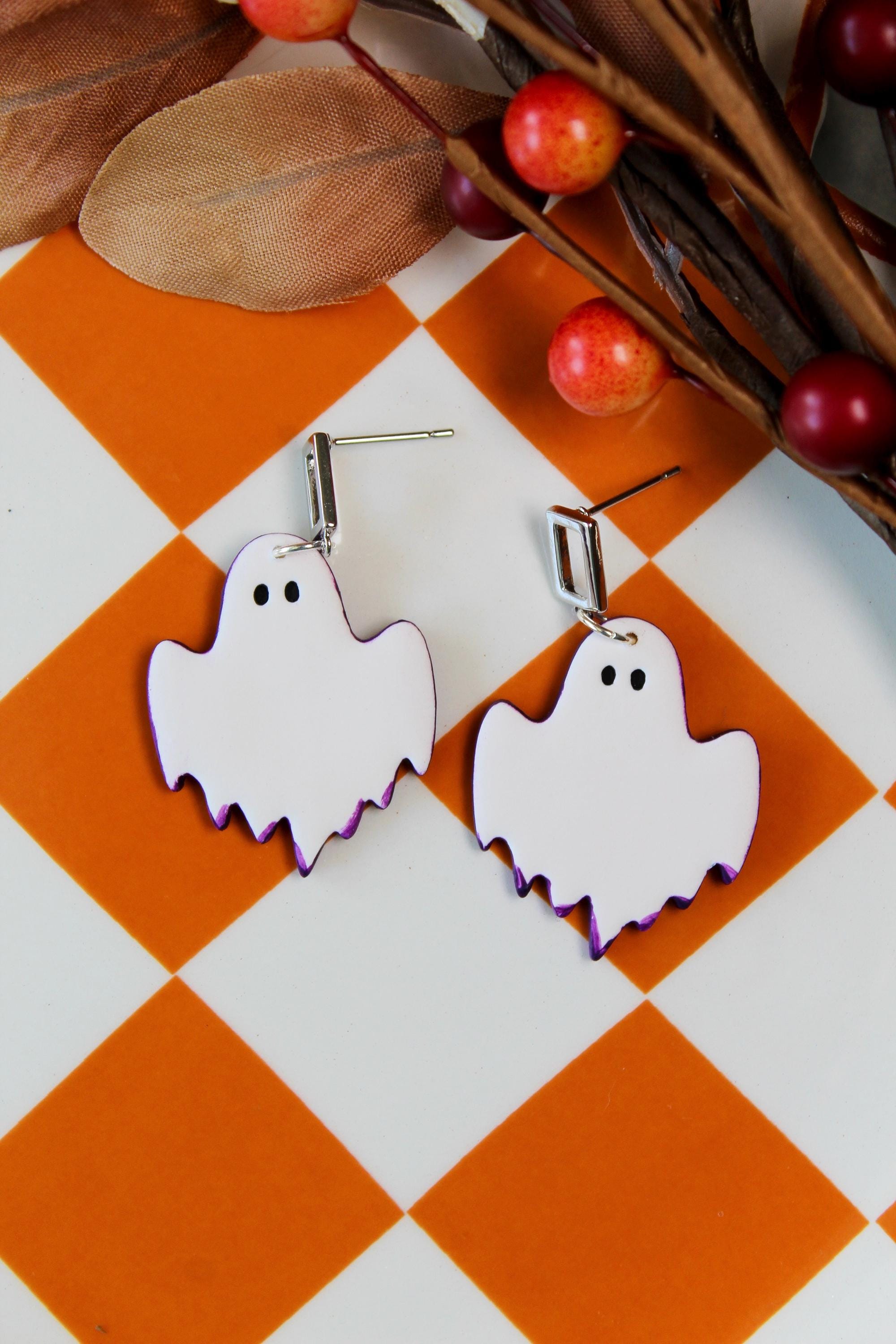 Ghost-shaped earrings on an orange and white checkered background with leaves and berries.