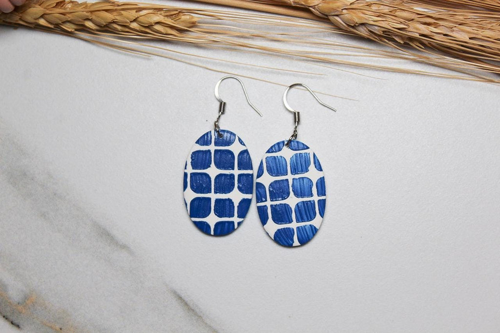 Blue and white patterned earrings on a light gray surface with dried wheat.