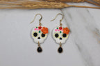 Pair of sugar skull earrings with floral details on a marble surface.