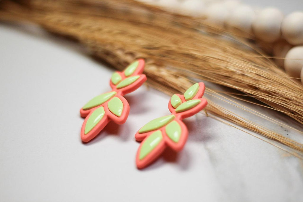 Neon green and pink leaf-shaped earrings on a neutral background with natural elements.