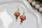 Pair of floral bouquet earrings on a white dish with a beige bead background