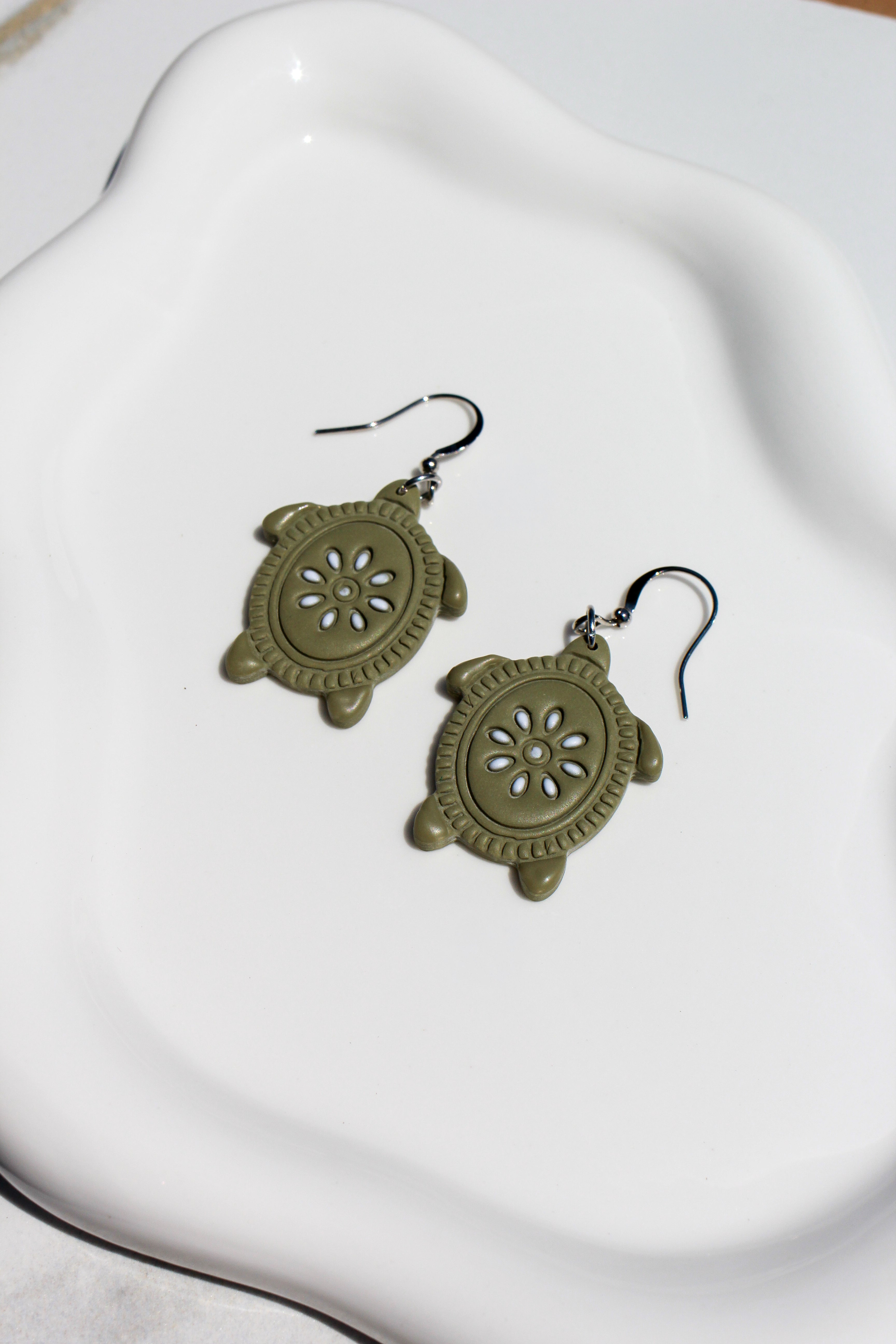 Pair of green turtle-shaped earrings on a white dish